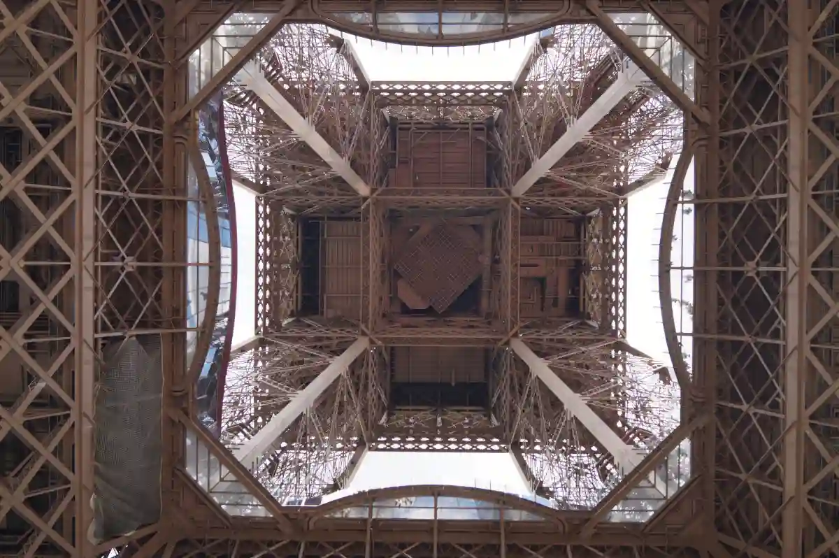 View from beneath the Eiffel Tower, showcasing its intricate iron lattice and massive beams stretching upwards to the top. View from beneath the Eiffel Tower, showcasing its intricate iron lattice and massive beams stretching upwards to the top.
