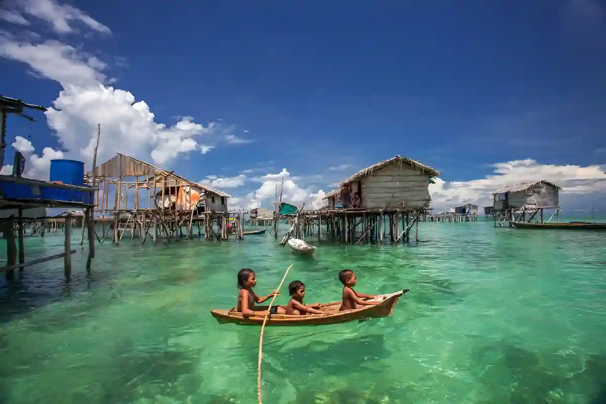 A Bajau Laut family on a traditional boat, gliding across the clear waters of Semporna, Sabah, with stilt homes in the background. A Bajau Laut family on a traditional boat, gliding across the clear waters of Semporna, Sabah, with stilt homes in the background.