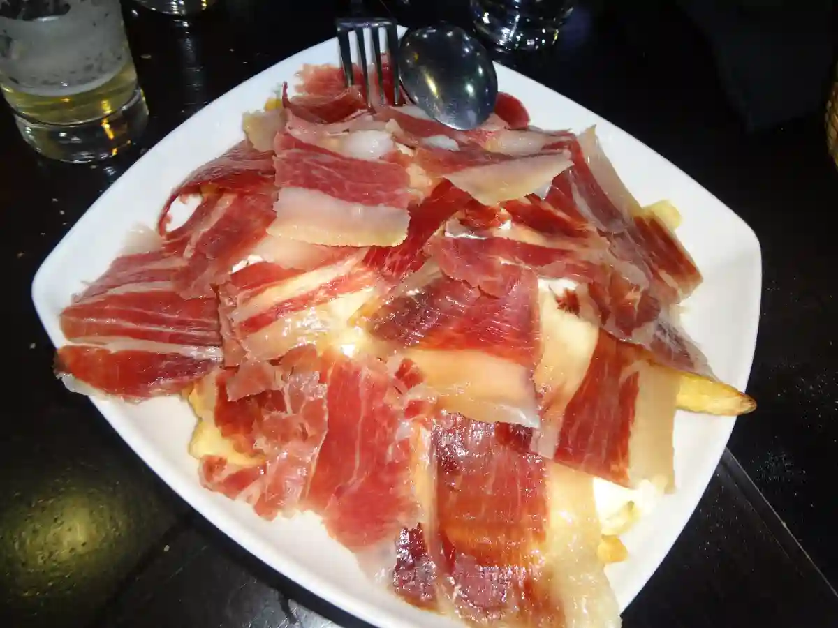 Thin slices of Jamón Ibérico arranged on a plate, showcasing the marbled texture and rich color. Thin slices of Jamón Ibérico arranged on a plate, showcasing the marbled texture and rich color.