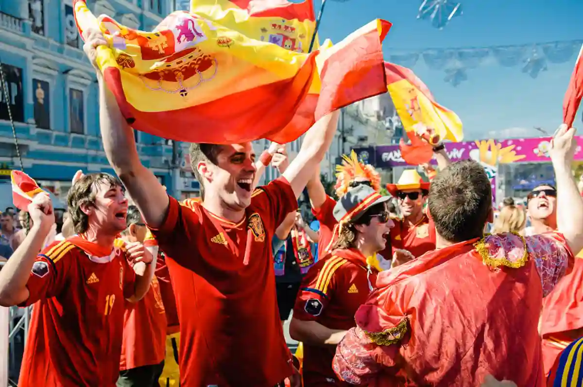 A group of passionate Spanish football fans in red and yellow jerseys, waving flags and cheering in the stands. A group of passionate Spanish football fans in red and yellow jerseys, waving flags and cheering in the stands.