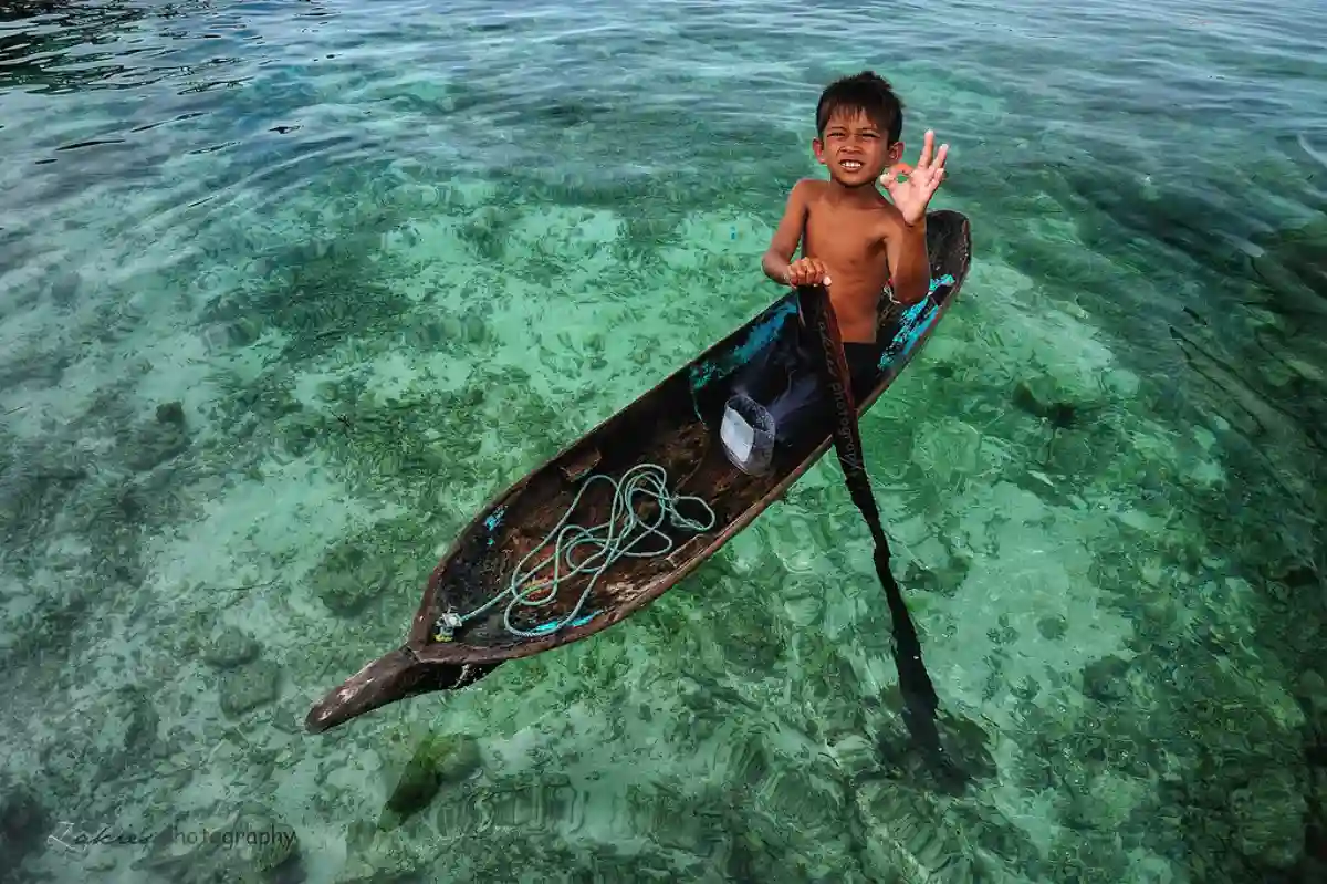 A young Bajau child, dressed in traditional attire, sitting on a boat, gazing out at the sea, embodying the spirit of the sea nomads. A young Bajau child, dressed in traditional attire, sitting on a boat, gazing out at the sea, embodying the spirit of the sea nomads.