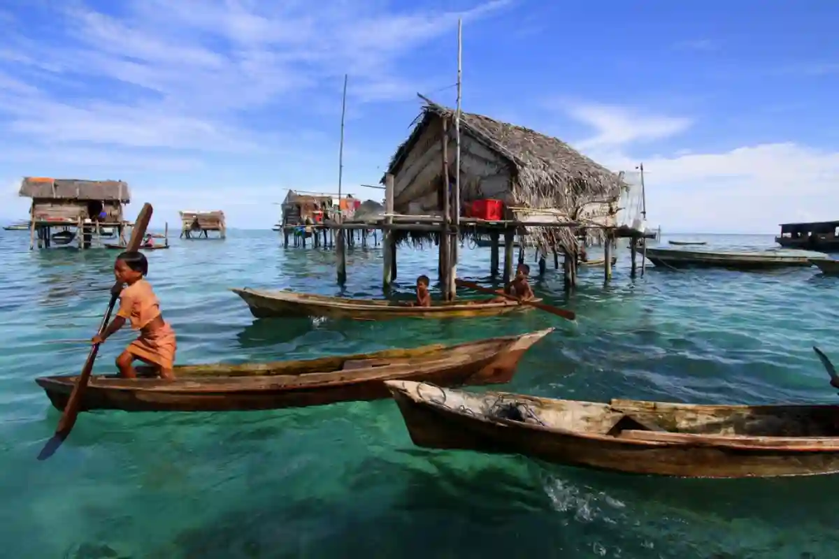 A Bajau sea nomad family in traditional boat, floating on the turquoise waters, surrounded by their stilt houses on the sea. A Bajau sea nomad family in traditional boat, floating on the turquoise waters, surrounded by their stilt houses on the sea.