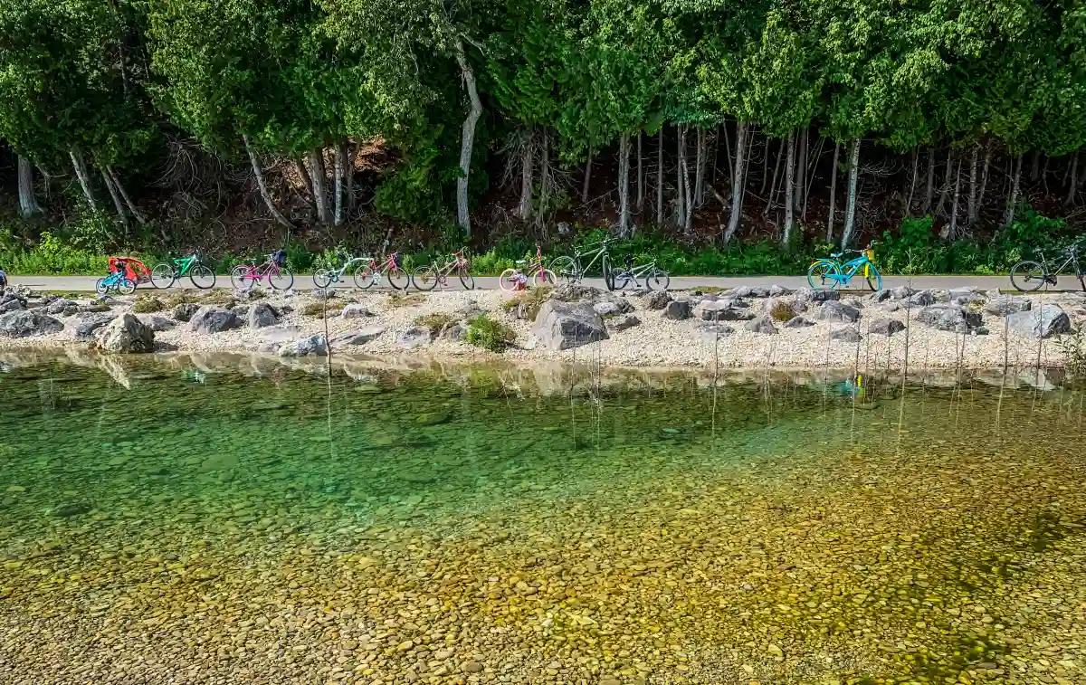 Bicycles parked beside the serene waters of Mackinac Island, with lush greenery and the iconic coastline in the background. Bicycles parked beside the serene waters of Mackinac Island, with lush greenery and the iconic coastline in the background.