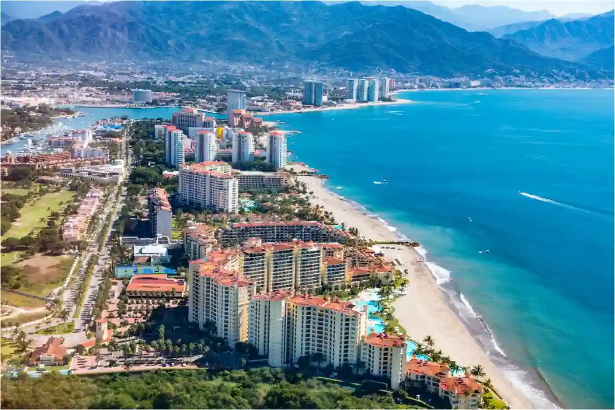 A closer aerial view of Puerto Vallarta, showcasing its golden beaches, vibrant town, and lush green hillsides surrounding the coastline. A closer aerial view of Puerto Vallarta, showcasing its golden beaches, vibrant town, and lush green hillsides surrounding the coastline.