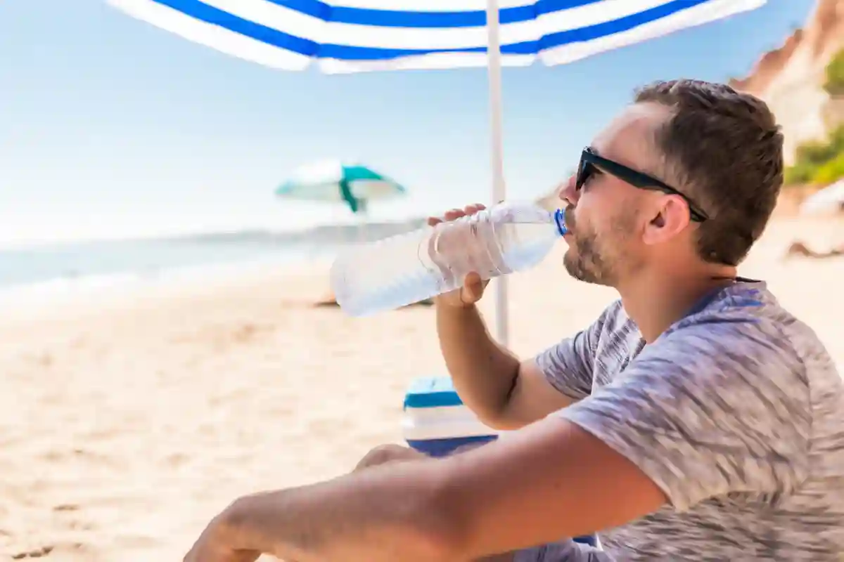 Young man under green solar umbrella drinks water on beach
Young man under green solar umbrella drinks water on beach