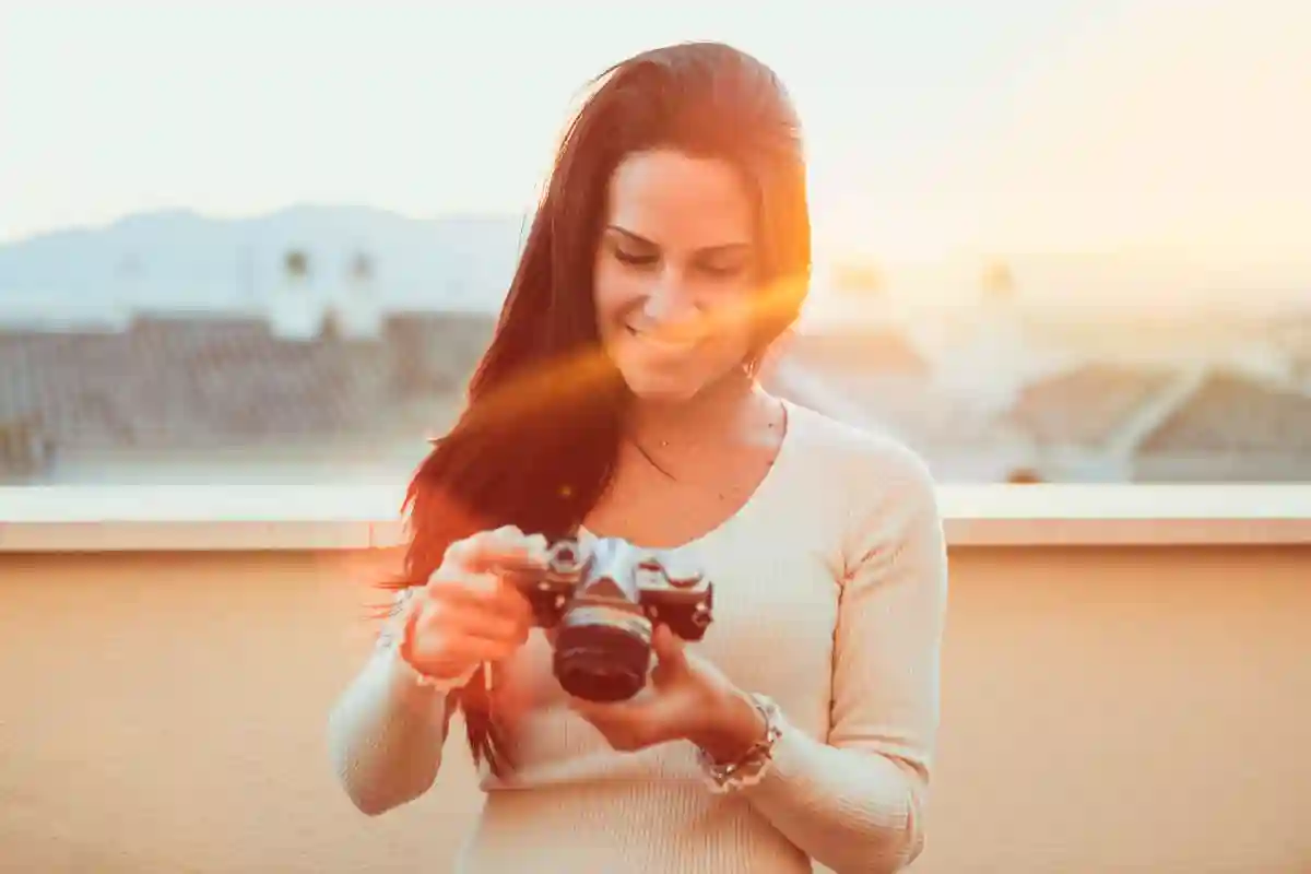 A young woman adjusting her vintage camera, silhouetted against the warm colors of a sunset. A young woman adjusting her vintage camera, silhouetted against the warm colors of a sunset.