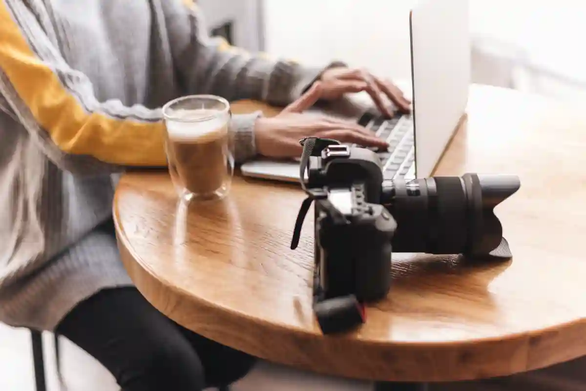 Close-up of a woman’s hands typing on a laptop in a cozy coffee shop setting, with a warm drink beside her. Close-up of a woman’s hands typing on a laptop in a cozy coffee shop setting, with a warm drink beside her.