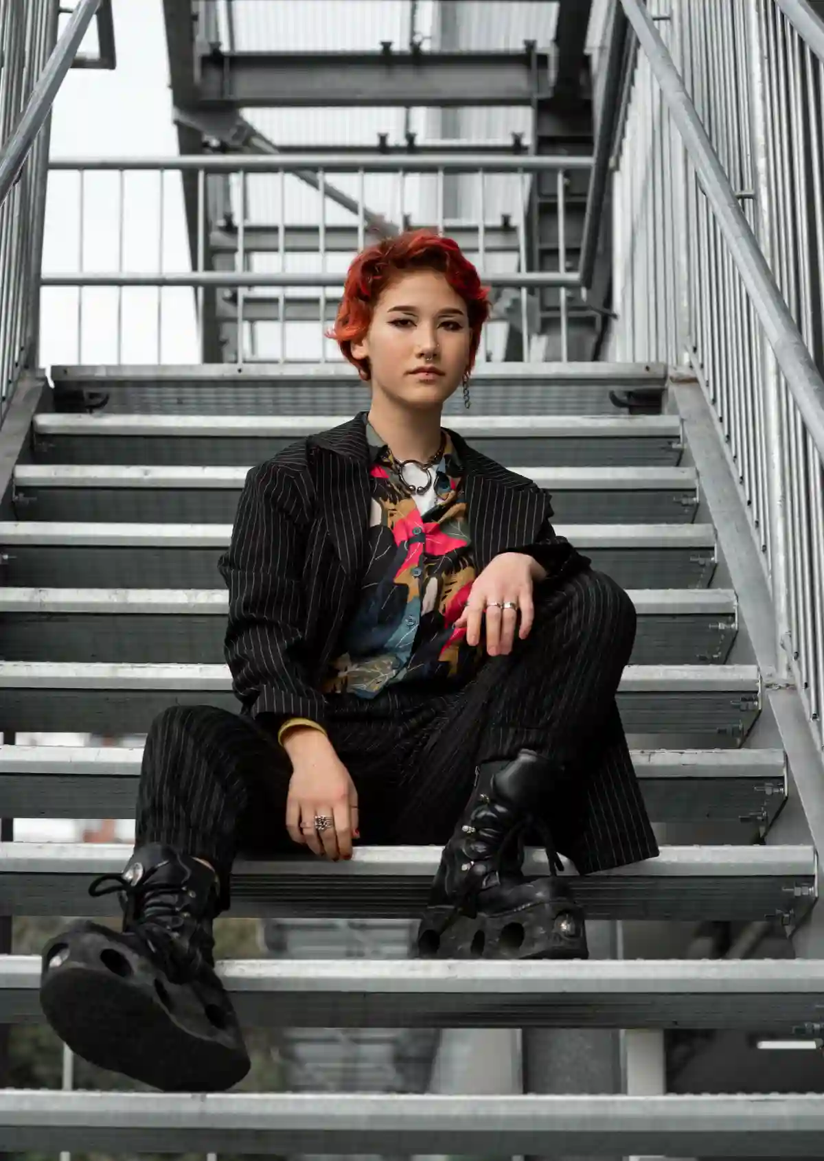 A redhead non-binary person sitting on stairs, wearing a relaxed, gender-neutral outfit consisting of a loose shirt, trousers, and sneakers, embodying confidence and comfort in their own identity. A redhead non-binary person sitting on stairs, wearing a relaxed, gender-neutral outfit consisting of a loose shirt, trousers, and sneakers, embodying confidence and comfort in their own identity.