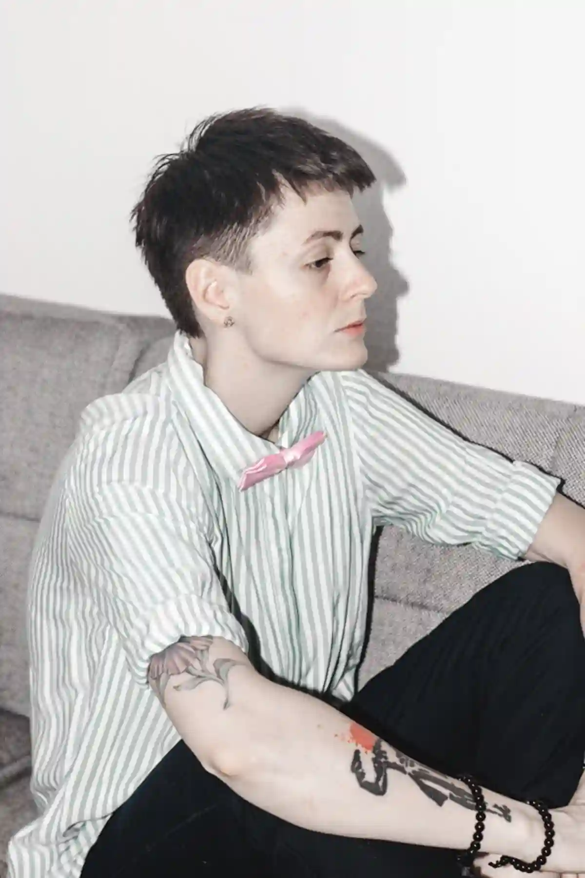 A tomboy person sitting on a sofa, facing to the side, dressed in a casual, comfortable outfit like a loose shirt, denim jeans, and sneakers, embodying a laid-back and confident style. A tomboy person sitting on a sofa, facing to the side, dressed in a casual, comfortable outfit like a loose shirt, denim jeans, and sneakers, embodying a laid-back and confident style.